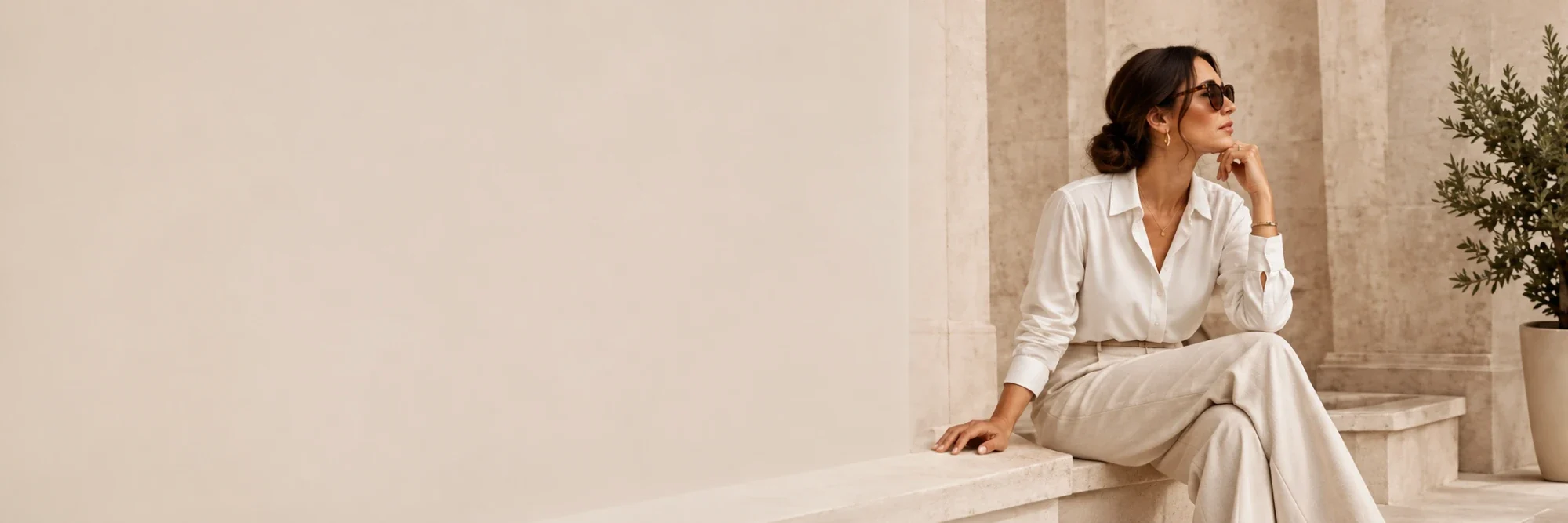 Woman in a white shirt and cream trousers sitting on a stone ledge